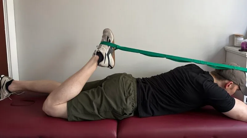 Me doing a quad stretch with a strap, lying on my stomach to increase the mobility of the muscles around my knee.