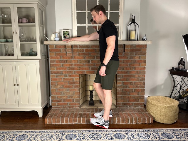 Demonstrating a step-down exercise on a stepper to strengthen the quad and patellar tendon for treating patellar tendonitis