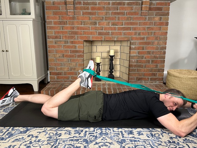 Demonstrating a prone quad stretch with a strap exercise to improve quadriceps flexibility for treating patellar tendonitis.