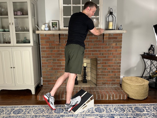Demonstrating a standing calf stretch on a slant board to stretch out the calf muscle