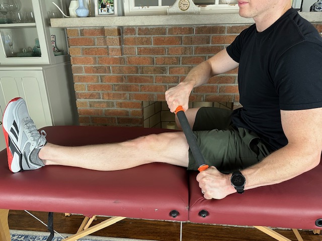 mobilizing the quadriceps muscle with a tiger tail, while sitting on a massage table, in order to treat patellar tendonitis