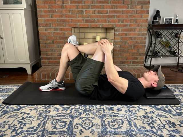Demonstrating a figure 4 piriformis stretch lying on a thick yoga mat
