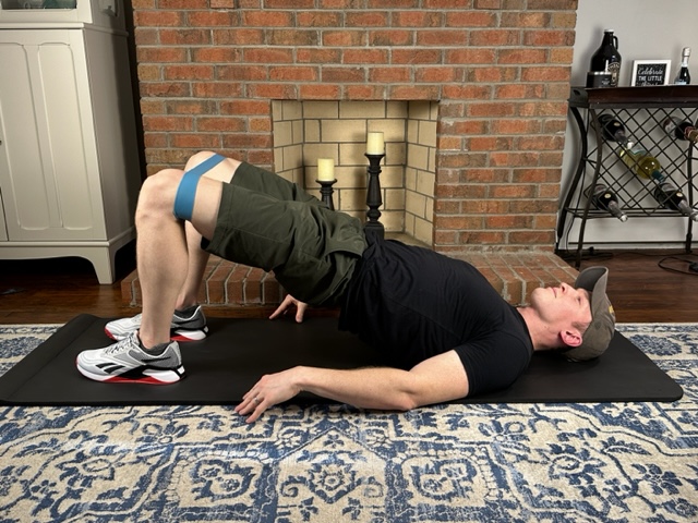 Demonstrating a bridge with band exercise to strengthen the butt and hip muscles for the treatment of Sinding-Larsen-Johansson