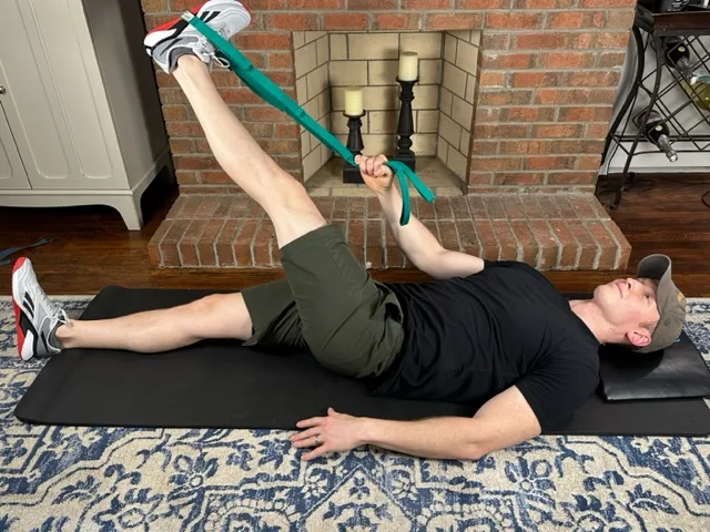 Demonstrating an ITB stretch with a strap to stretch out tight lateral hip muscles for treating distal ITB syndrome