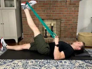 Physical therapist demonstrating hamstring stretch with strap performed at home after knee arthroscopy to improve flexibility and motion